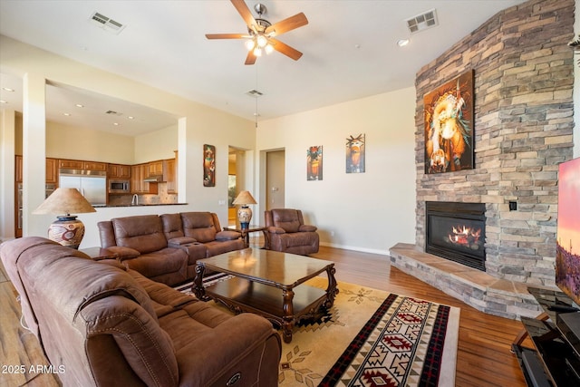 living room with ceiling fan, a stone fireplace, and light wood-type flooring