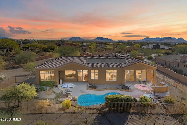 back house at dusk featuring a mountain view, solar panels, and a patio