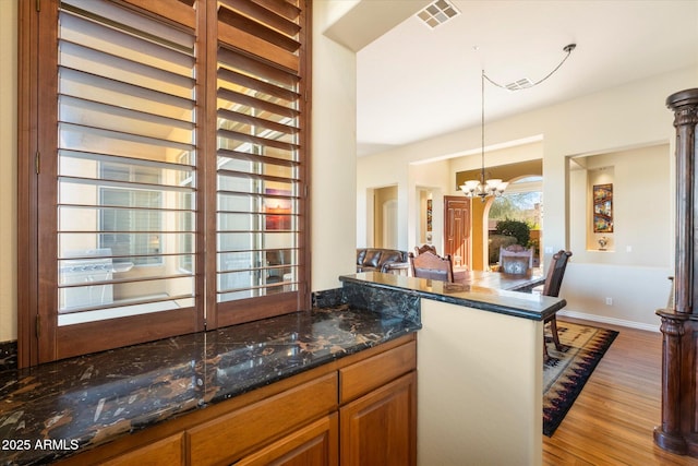 kitchen featuring pendant lighting, dark stone countertops, light wood-type flooring, and a chandelier