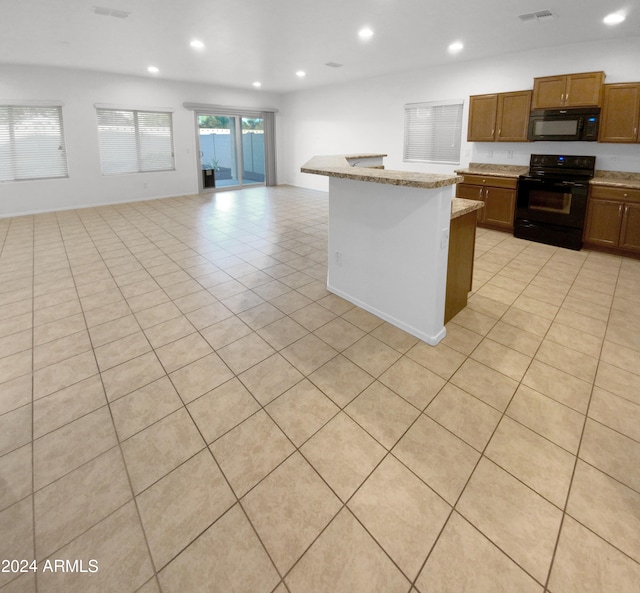 kitchen featuring black appliances, light tile patterned floors, a kitchen island, and light stone countertops