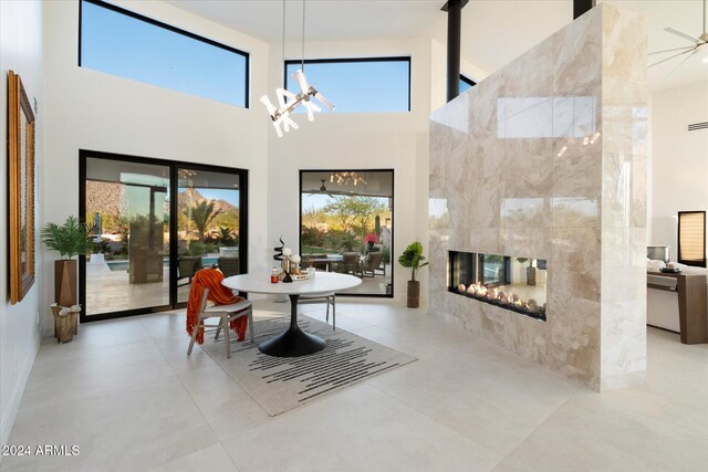 dining room featuring tile walls, a tiled fireplace, light tile patterned floors, and a high ceiling