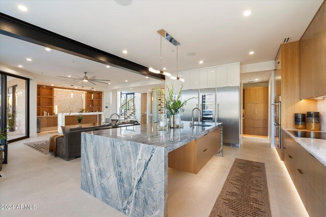 kitchen featuring a large island with sink, a breakfast bar, light stone countertops, pendant lighting, and sink