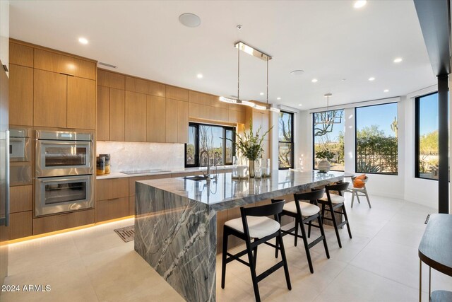 kitchen with black electric cooktop, light stone countertops, stainless steel double oven, light brown cabinetry, and sink