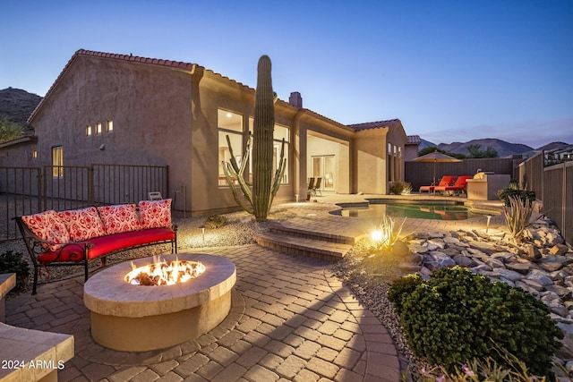 back house at dusk featuring a fenced in pool, a patio area, a mountain view, and a fire pit