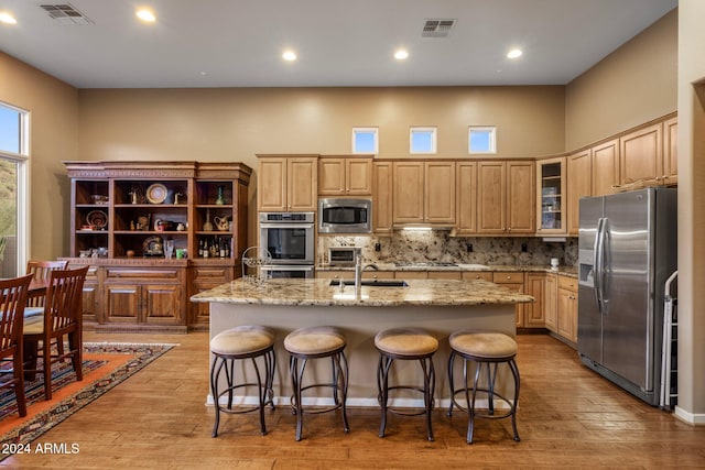 kitchen with appliances with stainless steel finishes, light hardwood / wood-style floors, a kitchen bar, and an island with sink