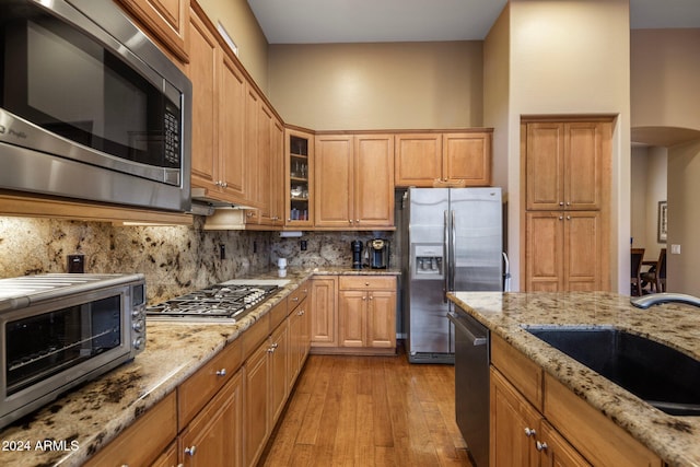 kitchen featuring tasteful backsplash, sink, light hardwood / wood-style floors, stainless steel appliances, and light stone counters