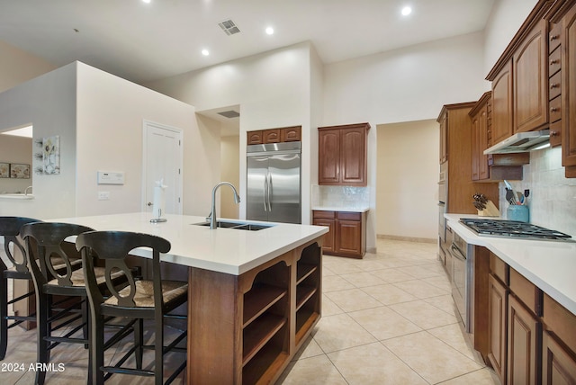 kitchen with sink, backsplash, stainless steel appliances, a center island with sink, and a kitchen breakfast bar