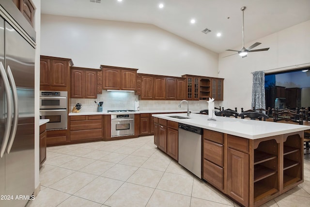 kitchen with ceiling fan, high vaulted ceiling, backsplash, stainless steel appliances, and a kitchen island with sink