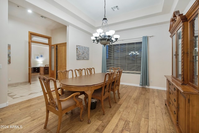 dining space with a raised ceiling, light hardwood / wood-style floors, and a chandelier