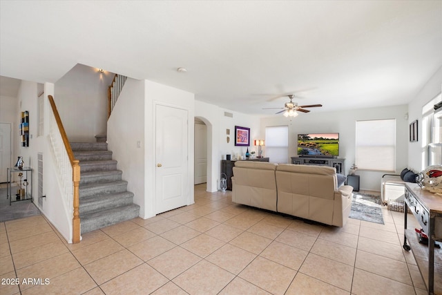 living area featuring ceiling fan, arched walkways, light tile patterned flooring, and stairs