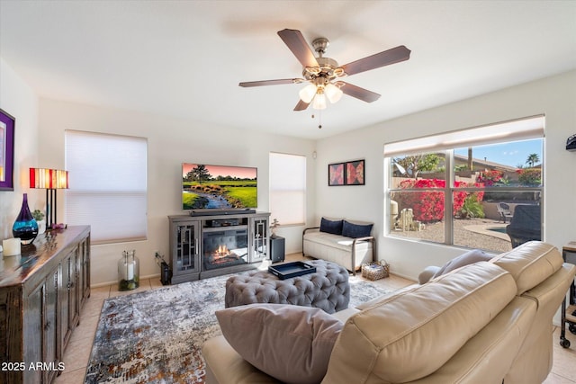 living area with light tile patterned floors, a glass covered fireplace, baseboards, and ceiling fan