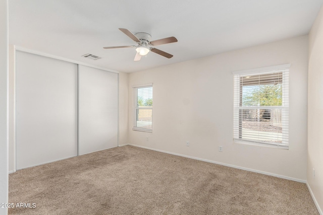 empty room featuring visible vents, carpet floors, and ceiling fan
