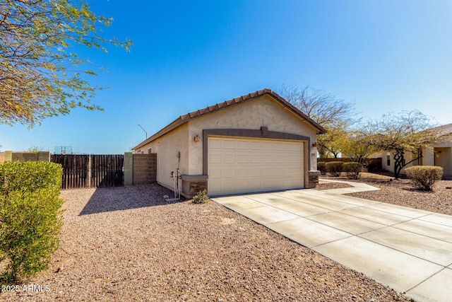 view of side of home with stucco siding, a tile roof, fence, concrete driveway, and an attached garage