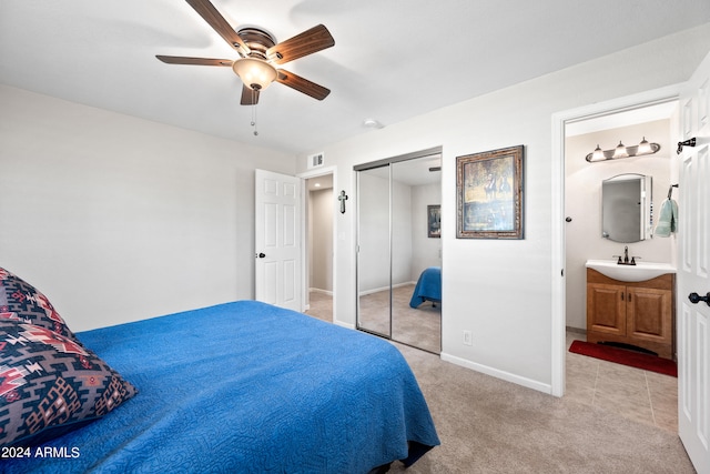 bedroom featuring connected bathroom, a closet, light carpet, sink, and ceiling fan