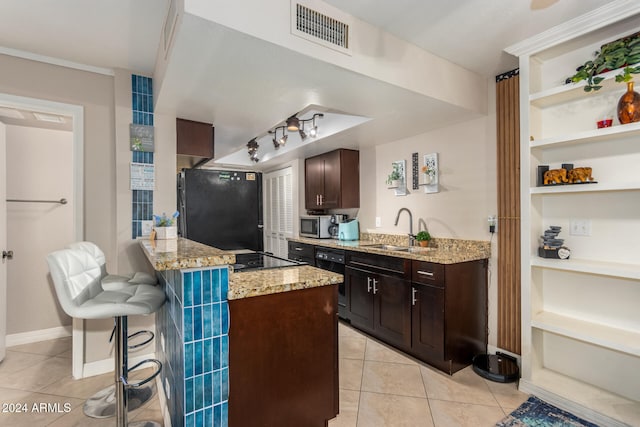 kitchen featuring light stone counters, a breakfast bar, dark brown cabinets, sink, and black appliances