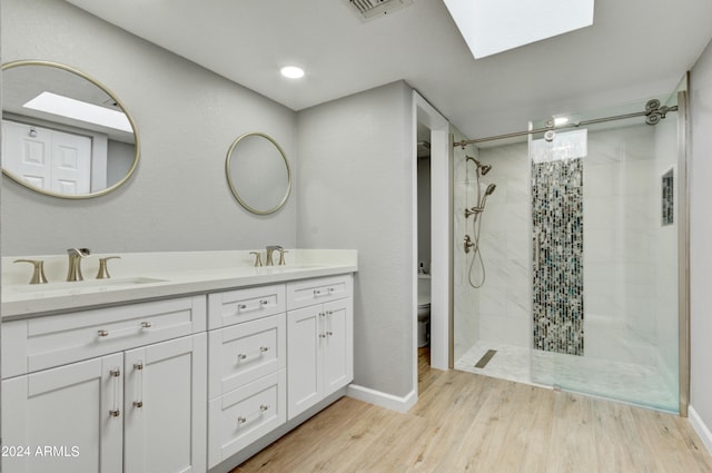 bathroom featuring a skylight, hardwood / wood-style flooring, toilet, a tile shower, and vanity