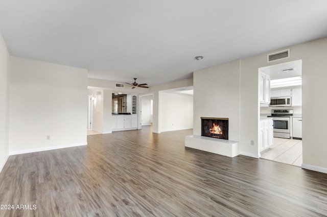 unfurnished living room featuring a large fireplace, ceiling fan, and light wood-type flooring