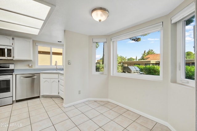 kitchen with plenty of natural light, light tile patterned floors, stainless steel appliances, and white cabinetry