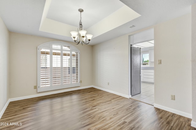 spare room with a healthy amount of sunlight, a chandelier, and light hardwood / wood-style floors