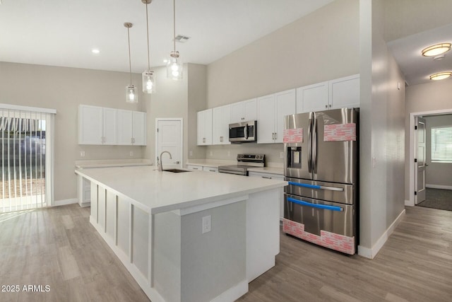 kitchen featuring stainless steel appliances, sink, pendant lighting, white cabinetry, and an island with sink