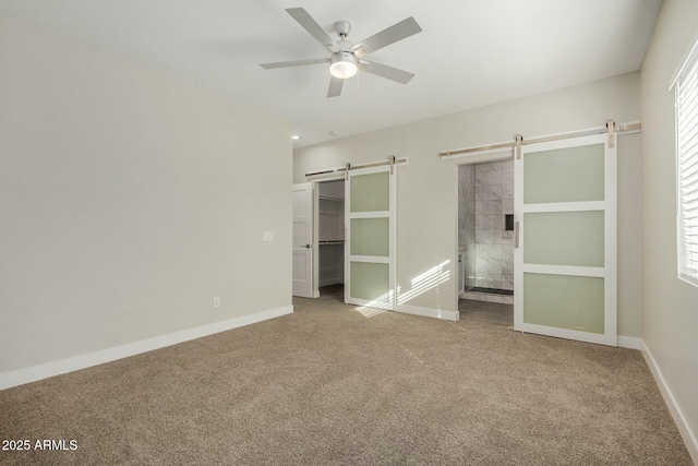 unfurnished bedroom featuring a barn door, ceiling fan, and carpet