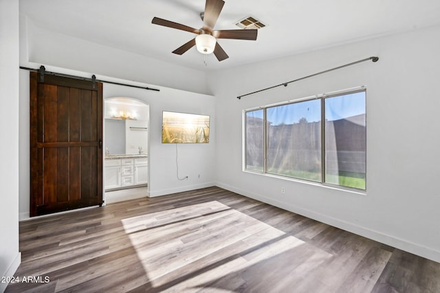 unfurnished bedroom with ensuite bath, ceiling fan, wood-type flooring, and a barn door