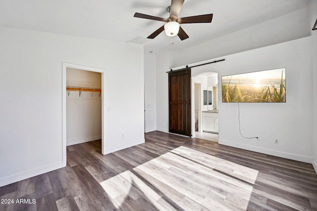 unfurnished bedroom with connected bathroom, ceiling fan, a barn door, wood-type flooring, and a walk in closet