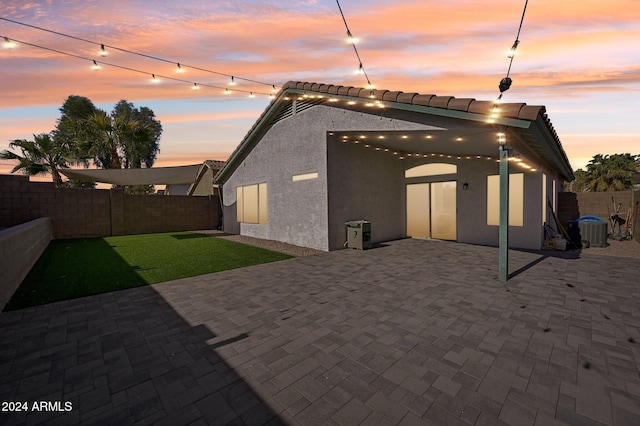 back house at dusk featuring central AC unit, a yard, and a patio