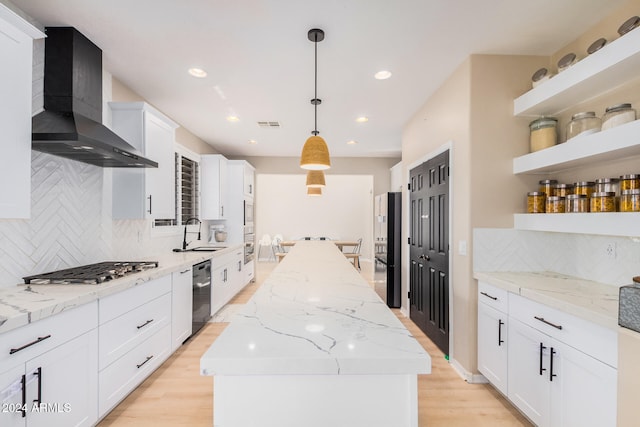 kitchen with wall chimney range hood, decorative light fixtures, light hardwood / wood-style floors, and a kitchen island