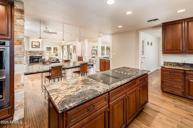 kitchen featuring visible vents, dark stone counters, a kitchen island, black electric stovetop, and light wood-style floors