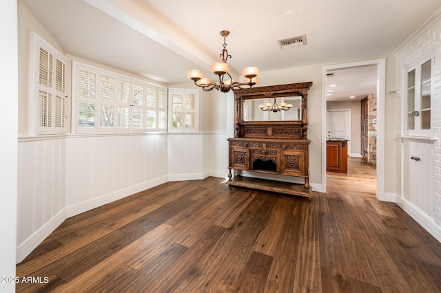 unfurnished living room with dark wood-style flooring, a wainscoted wall, visible vents, a chandelier, and baseboards