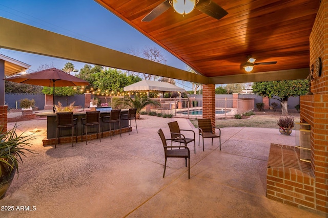 view of patio with outdoor dry bar, a fenced backyard, a fenced in pool, and a ceiling fan