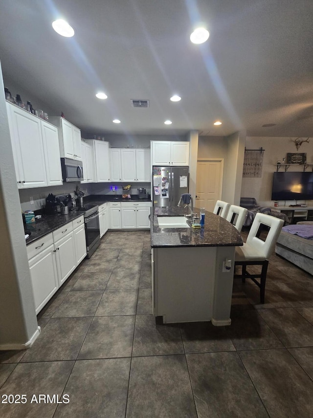 kitchen with white cabinetry, sink, dark tile patterned flooring, a kitchen island with sink, and stainless steel appliances