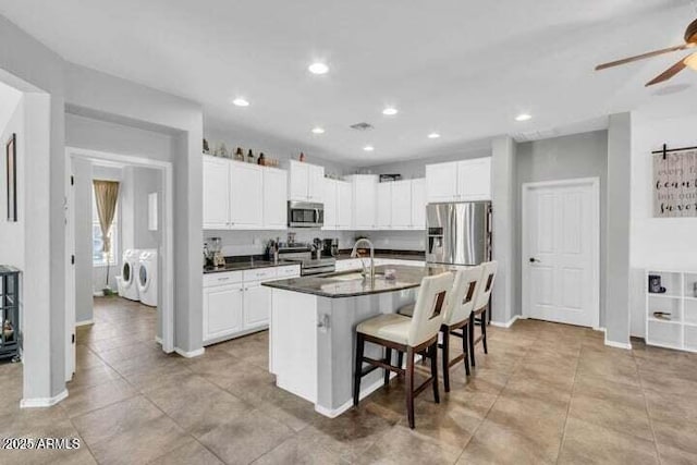 kitchen featuring washer and dryer, a breakfast bar, sink, a kitchen island with sink, and stainless steel appliances