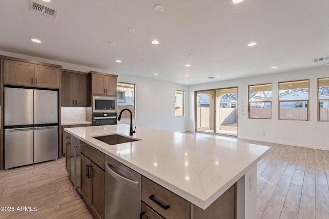 kitchen with sink, stainless steel appliances, light hardwood / wood-style flooring, and an island with sink