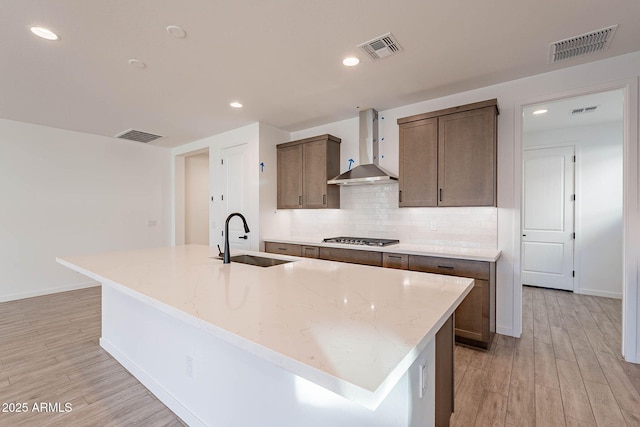 kitchen with stainless steel gas stovetop, tasteful backsplash, a kitchen island with sink, sink, and wall chimney exhaust hood