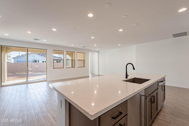 kitchen with light stone countertops, sink, a center island with sink, and light wood-type flooring