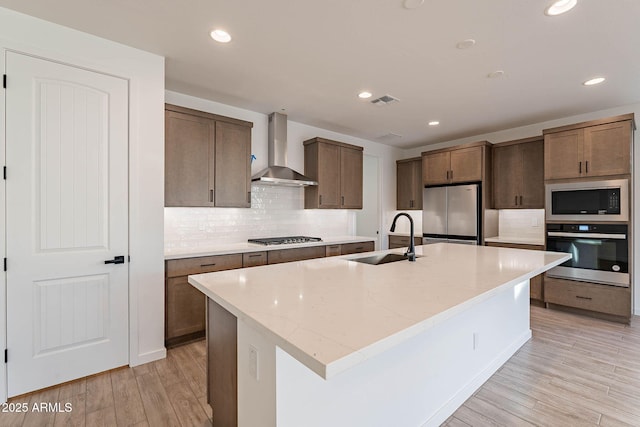 kitchen featuring sink, a center island with sink, wall chimney range hood, and stainless steel appliances