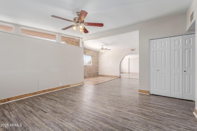 spare room featuring brick wall, visible vents, arched walkways, and wood finished floors