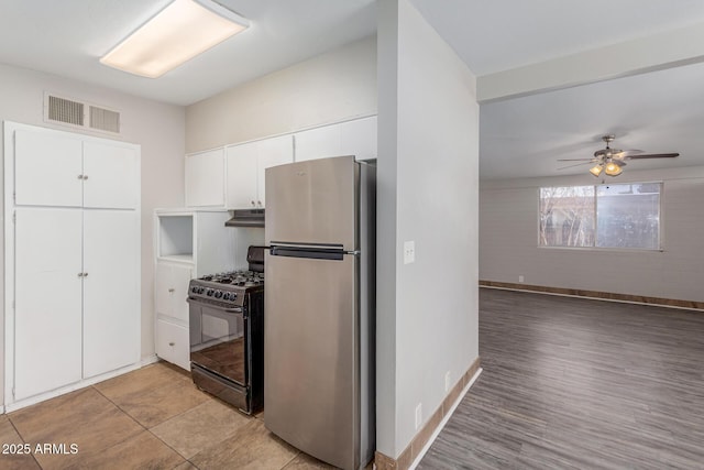 kitchen with black gas range, visible vents, freestanding refrigerator, under cabinet range hood, and white cabinetry