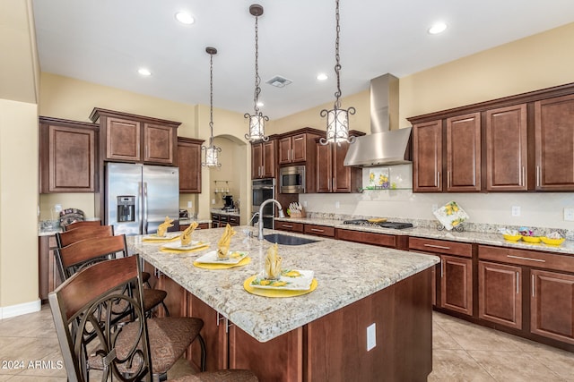 kitchen featuring wall chimney exhaust hood, appliances with stainless steel finishes, a center island with sink, and sink