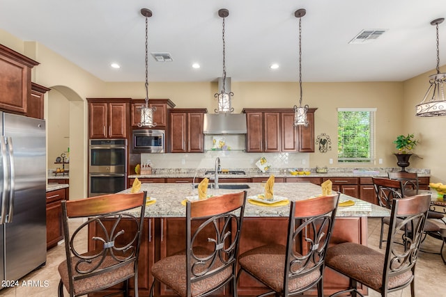 kitchen featuring a center island with sink, pendant lighting, stainless steel appliances, and a breakfast bar