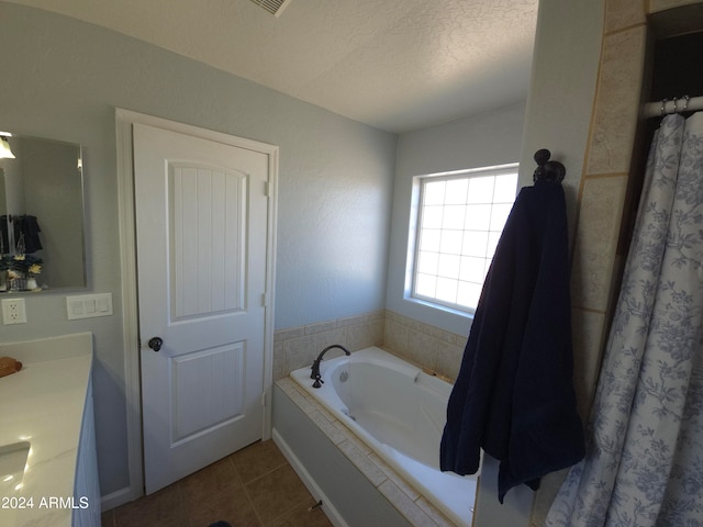 bathroom featuring tiled bath, tile patterned flooring, a textured ceiling, and vanity