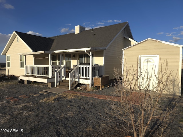 back of property with a porch, a shingled roof, an outdoor structure, a shed, and a chimney