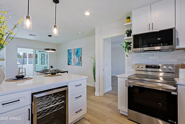 kitchen featuring decorative light fixtures, beverage cooler, white cabinets, and appliances with stainless steel finishes