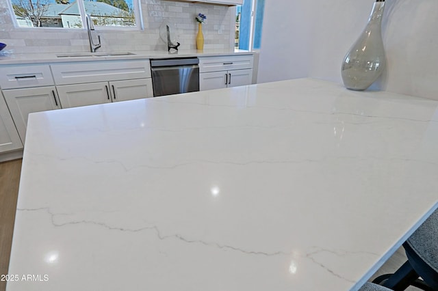 kitchen with sink, tasteful backsplash, white cabinetry, dishwasher, and light stone countertops