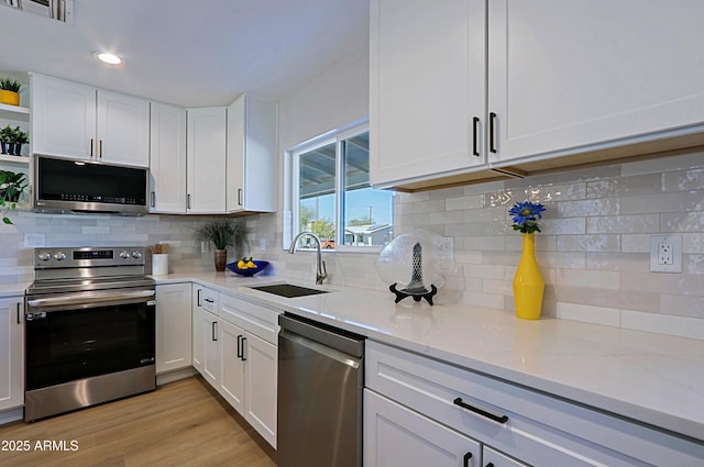 kitchen with appliances with stainless steel finishes, white cabinetry, sink, light stone counters, and light hardwood / wood-style floors