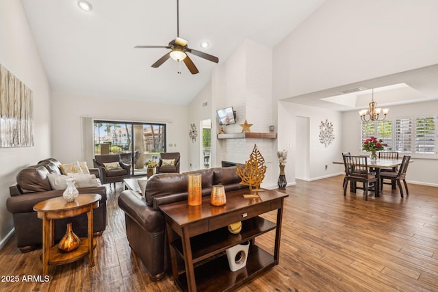 living room featuring ceiling fan with notable chandelier, high vaulted ceiling, a fireplace, and hardwood / wood-style floors