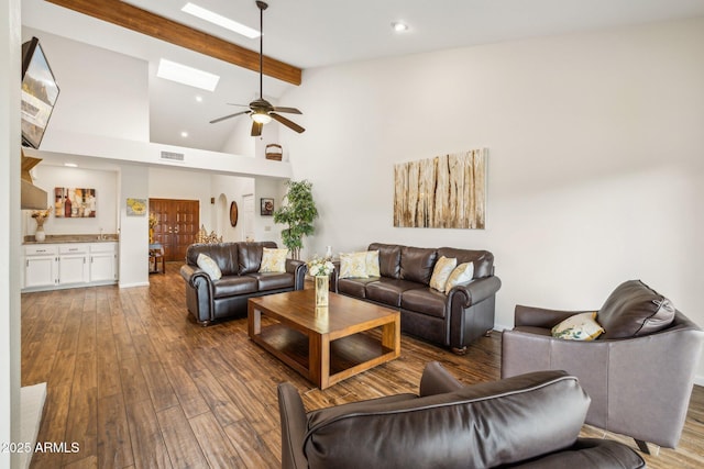 living room featuring high vaulted ceiling, ceiling fan, dark wood-type flooring, a skylight, and beamed ceiling