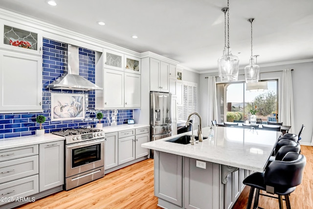 kitchen with stainless steel appliances, a sink, light wood-style floors, ornamental molding, and wall chimney exhaust hood